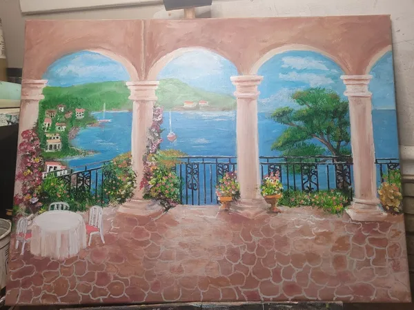 Pink arches and columns frame a flower-filled terrace with a table, chairs and iron railing overlooking a blue bay, sailboats and green coastal hills.