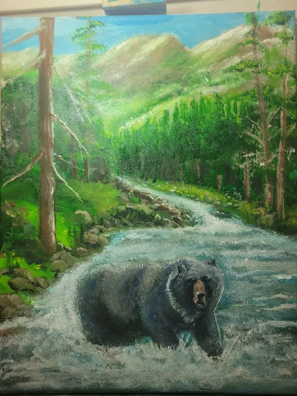 Large black bear in white river rapids with dense green forest and mountains in the background.