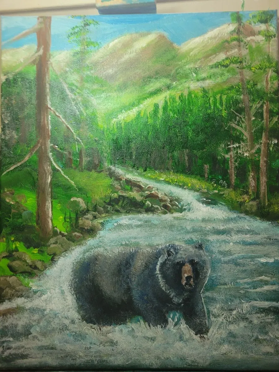 Large black bear in white river rapids with dense green forest and mountains in the background.