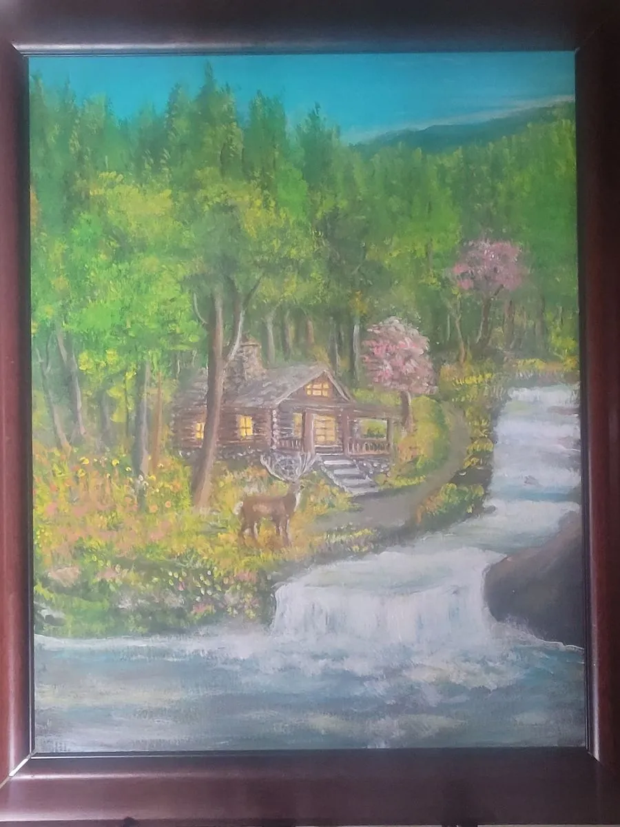 Log cabin with illuminated windows, a deer and flowering trees beside a cascading woodland waterfall.